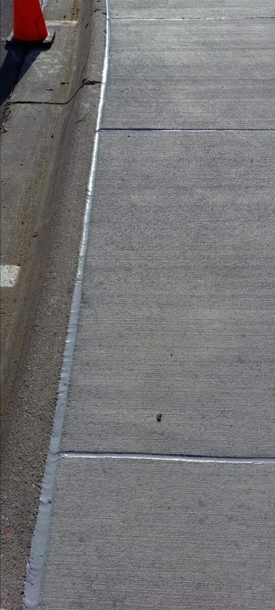 Freshly sealed sidewalk joint at the curb line in Omaha